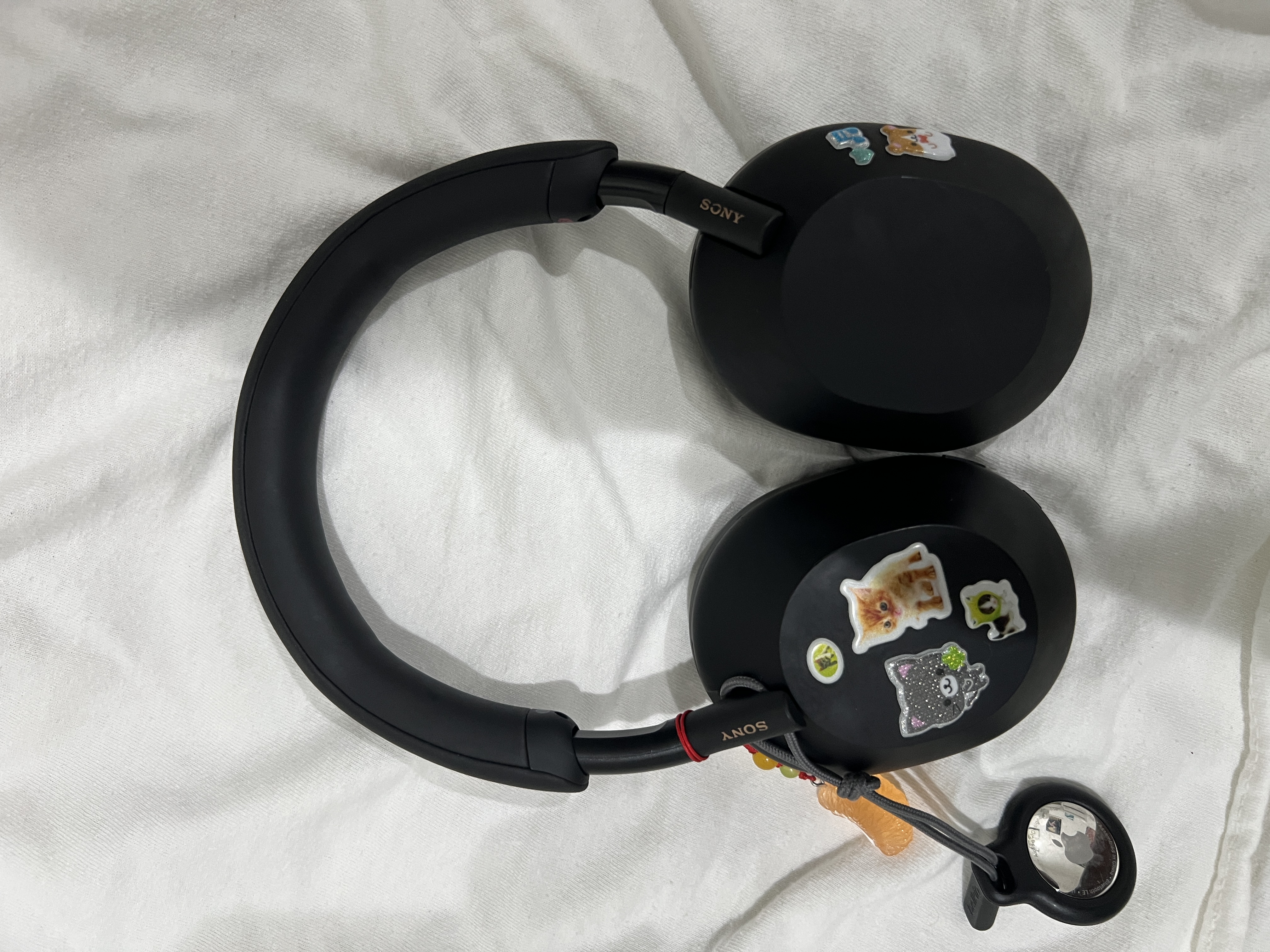 Black, Sony WH-1000XM5 Headphones covered in various puffy stickers.