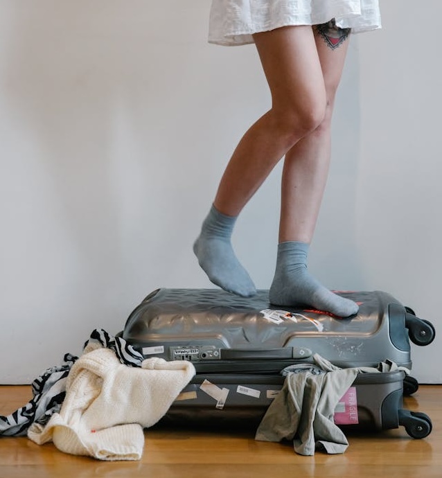 Woman standing on suitcase bursting with clothes.